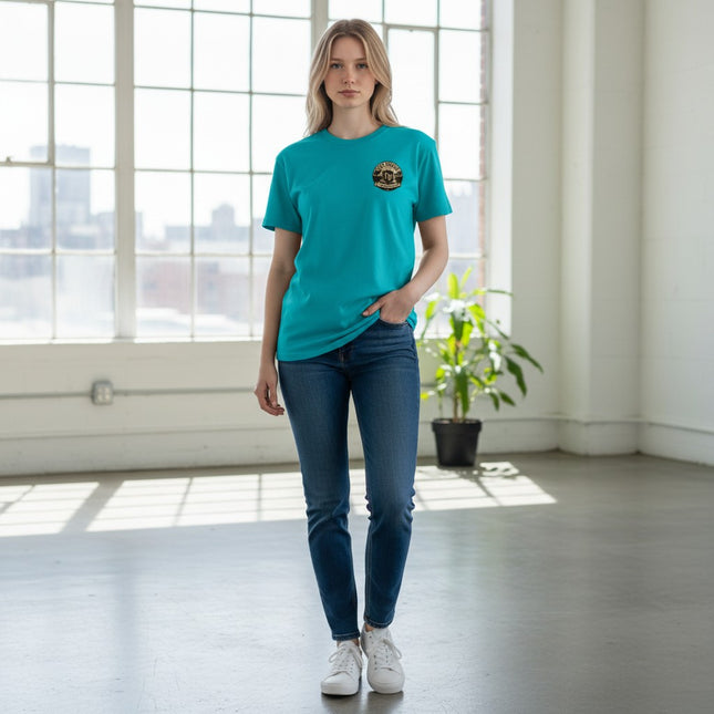 Woman wearing a teal Fort Denaud Beard and Skin cotton logo t-shirt with dark blue jeans in a bright studio.
