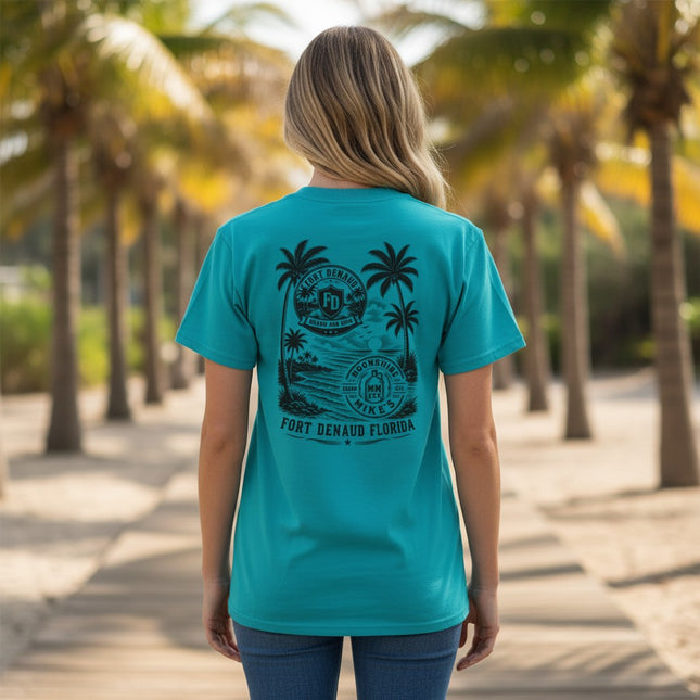 Woman wearing a teal Fort Denaud Beard and Skin cotton t-shirt with a black tropical logo graphic on the back